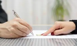 Due mani su un documento legale, una firma mentre l’altra indica una fede nuziale